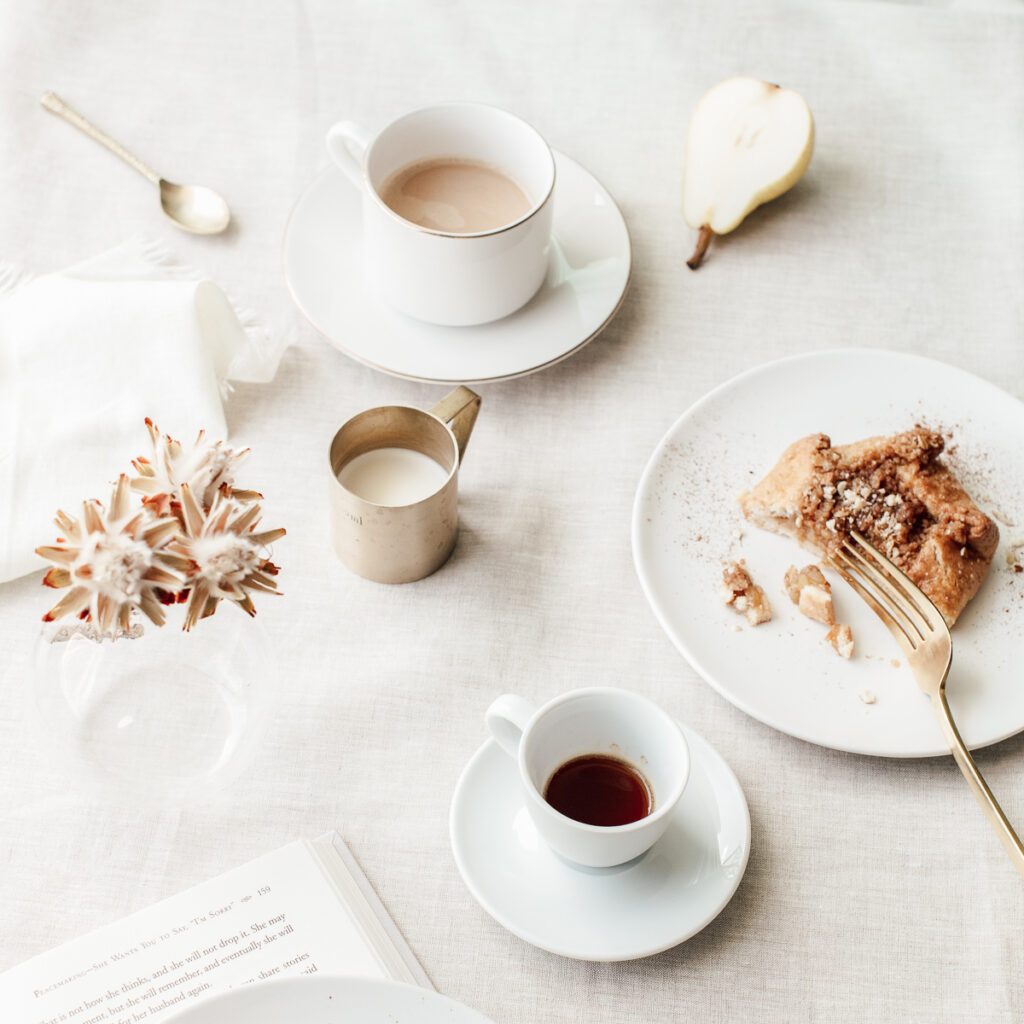A cup of tea on a white fabric table cloth, with a half eaten pastry on the right on a white plate, with a golden fork on the side. highlighting Great Habits To Start