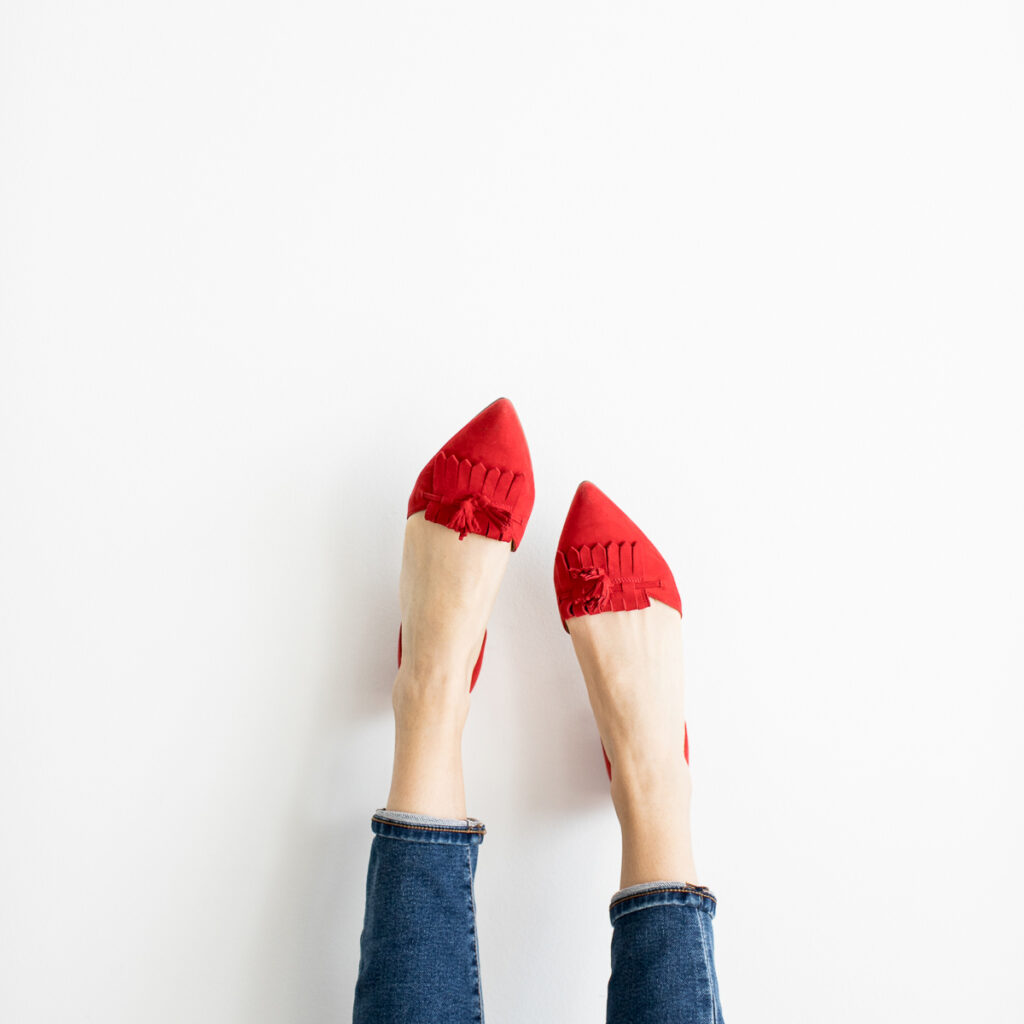 An image that you would use when creating pins, a womens legs against a wall wearing bright red pumps.