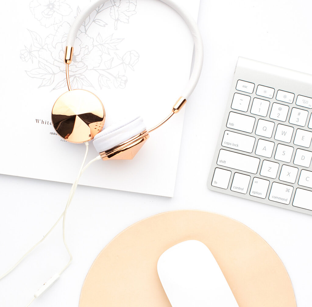 Marketing 101: How To Promote Your Blog With Google Ads desk set up with a set of gold headphones on a white background next to a mac keyboard.