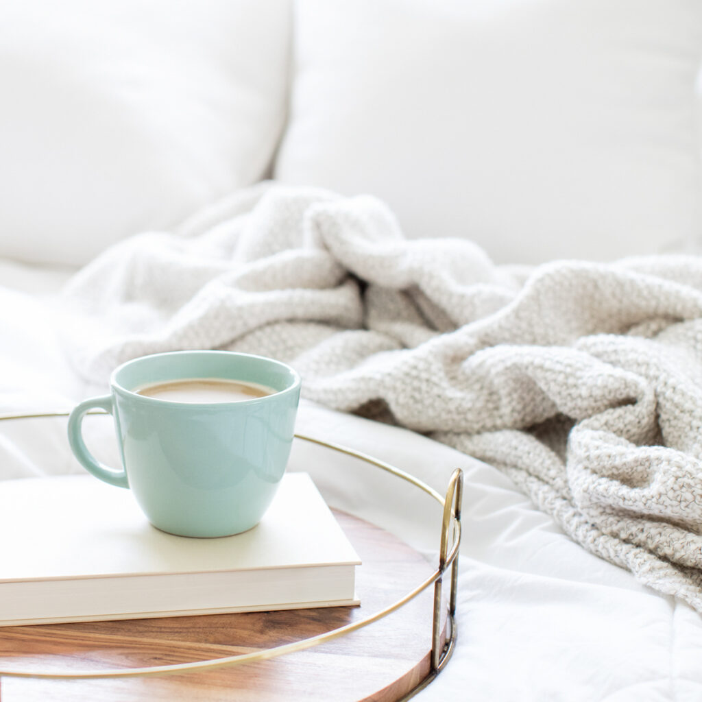 A green coffee cup on a white book, on a neutral sofa. Book containing Tips For Growing Your Brand